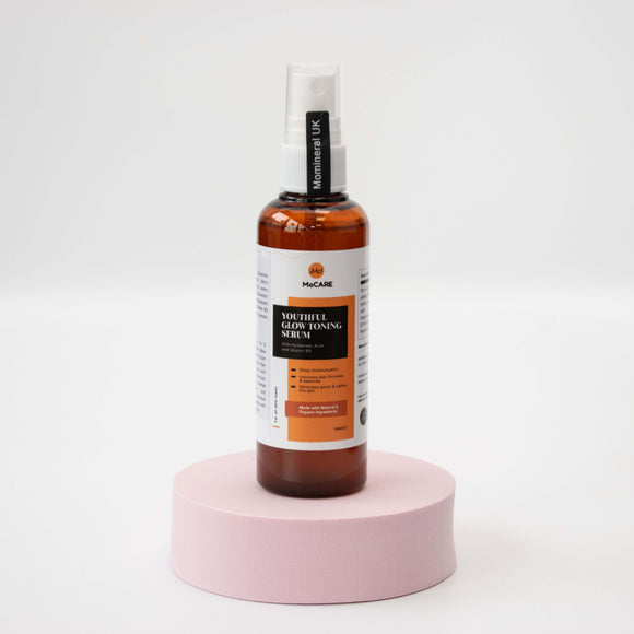 Bottle of Nourish Glow Toning Serum on a pink stand with a white background