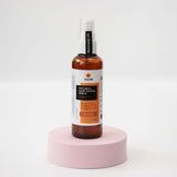 Bottle of Nourish Glow Toning Serum on a pink stand with a white background